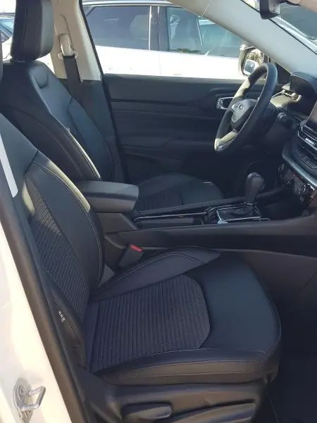 Vue intérieure côté conducteur du Jeep Compass blanc 2024, sièges noirs, accoudoir central et tableau de bord avec écran tactile.