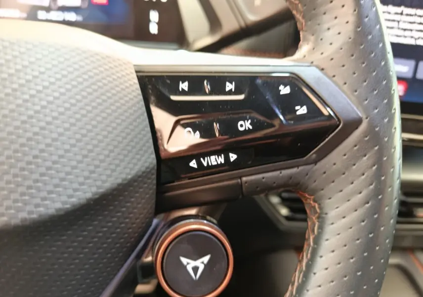 Gros plan sur le volant cuir perforé avec surpiqûres orange et commandes tactiles du CUPRA BORN gris foncé 2023.