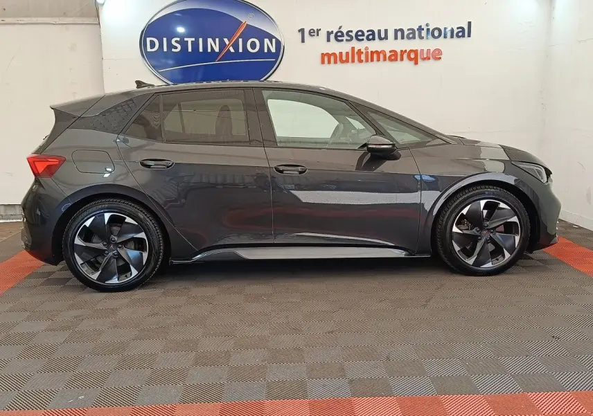 Profil droit de la CUPRA BORN 230ch gris foncé électrique 2023 avec jantes noires et logo distinctif sur roue.