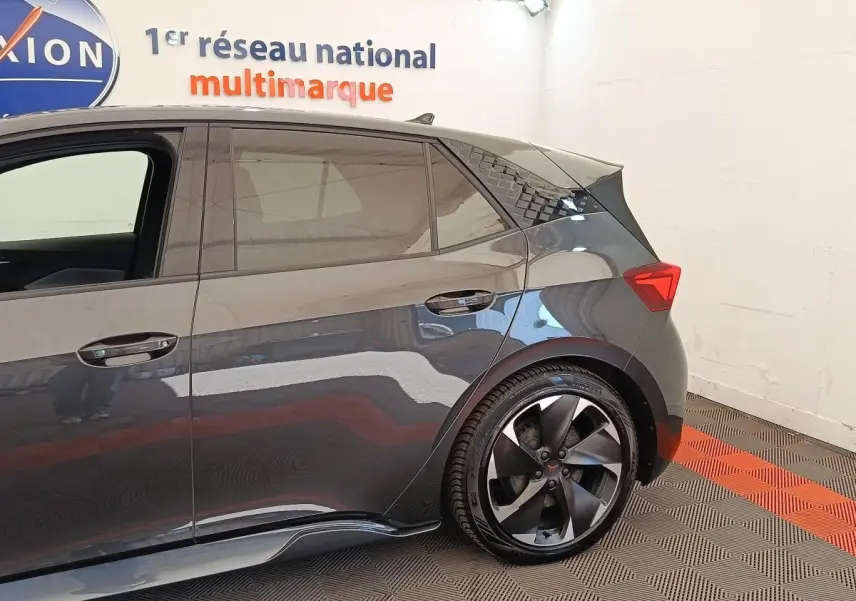 Vue latérale droite du CUPRA Born gris foncé, mettant en valeur la roue arrière et les lignes dynamiques du véhicule.