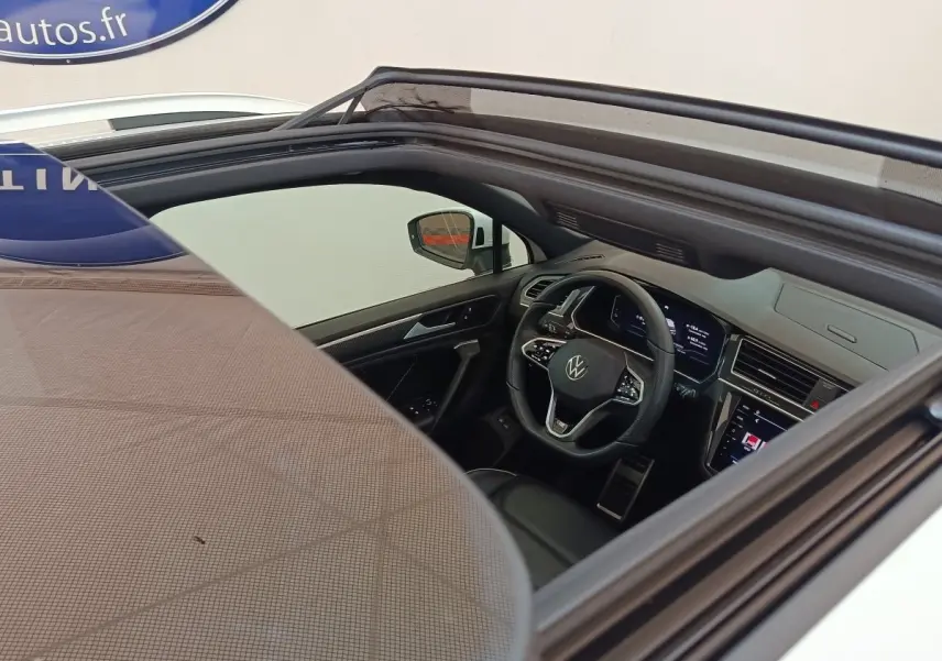 Vue intérieure par le toit ouvrant du Volkswagen Tiguan blanc 2023, montrant le volant multifonctions et le tableau de bord digital.