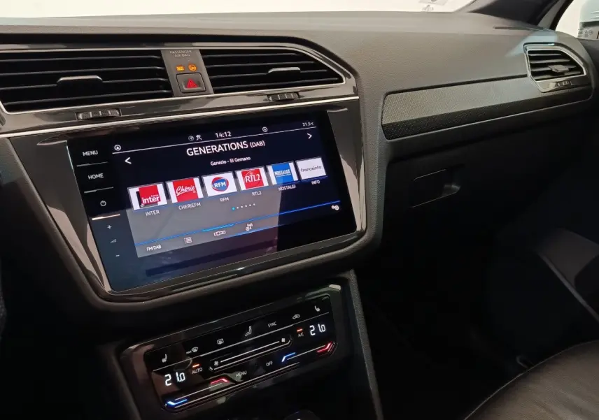 Vue intérieure du tableau de bord du Volkswagen Tiguan blanc 2023, écran tactile central et commandes climatisation visibles.