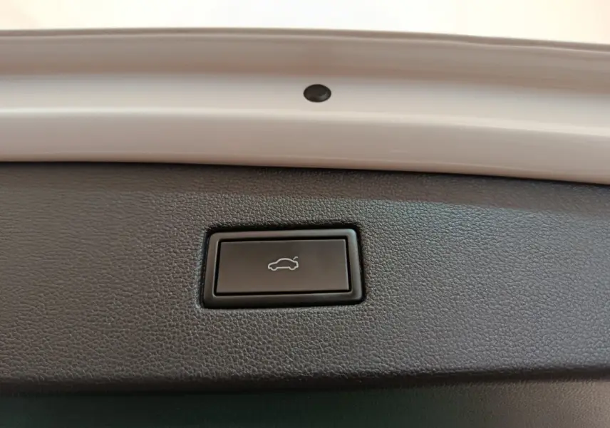 Bouton noir d'ouverture électrique du coffre sur la partie intérieure du hayon d'un Volkswagen Tiguan blanc.
