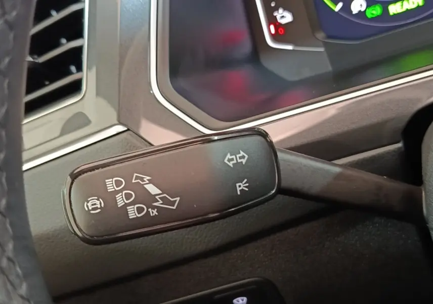 Gros plan sur la manette de clignotant et feux du Volkswagen Tiguan hybride, tableau de bord numérique en arrière-plan.