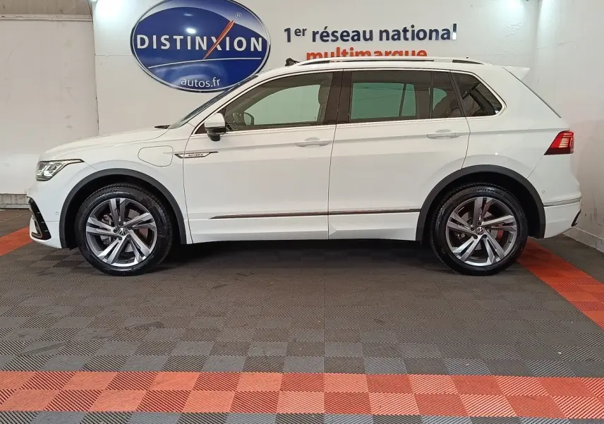 Profil droit d'un Volkswagen Tiguan blanc 2023 hybride rechargeable finition R-Line Exclusive avec jantes alliage et toit ouvrant.