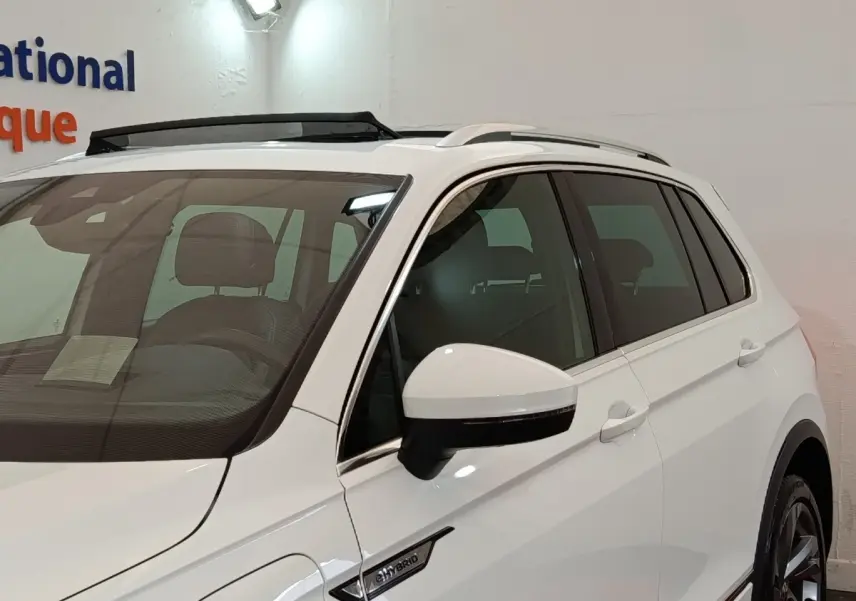 Vue 3/4 avant droit du Volkswagen Tiguan blanc hybride rechargeable avec badge eHybrid et toit ouvrant électrique visible.