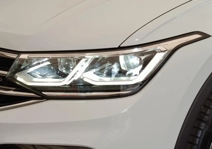 Gros plan sur le phare avant droit blanc du Volkswagen Tiguan 1.4 eHybrid 2023 avec signature lumineuse LED distinctive.