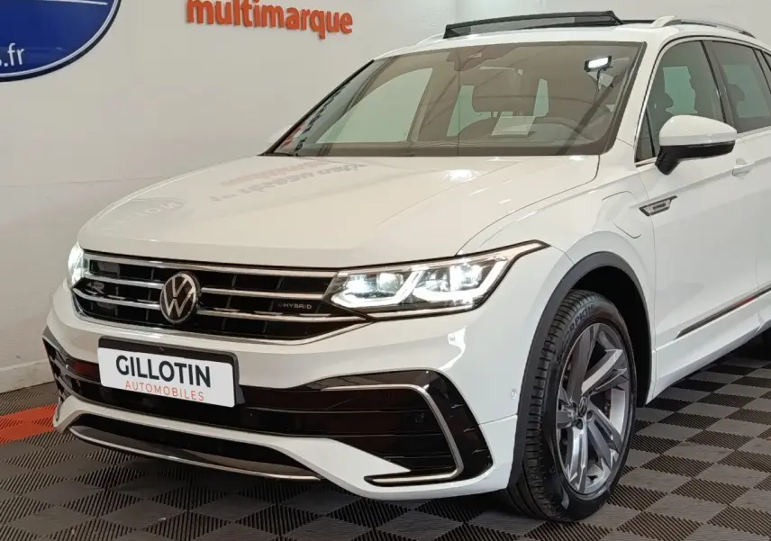 Vue 3/4 avant d'un Volkswagen Tiguan blanc hybride rechargeable avec calandre R-Line et jantes alliage grises.