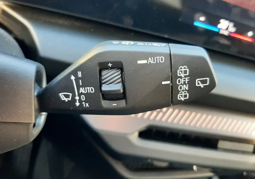 Gros plan sur la commande des essuie-glaces à gauche du volant dans l'habitacle noir d'une BMW Série 1 120D 2025.