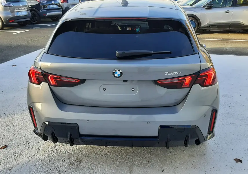 Vue arrière d'une BMW Série 1 120d gris Skyscraper avec feux LED et diffuseur noir sportif sur parking.