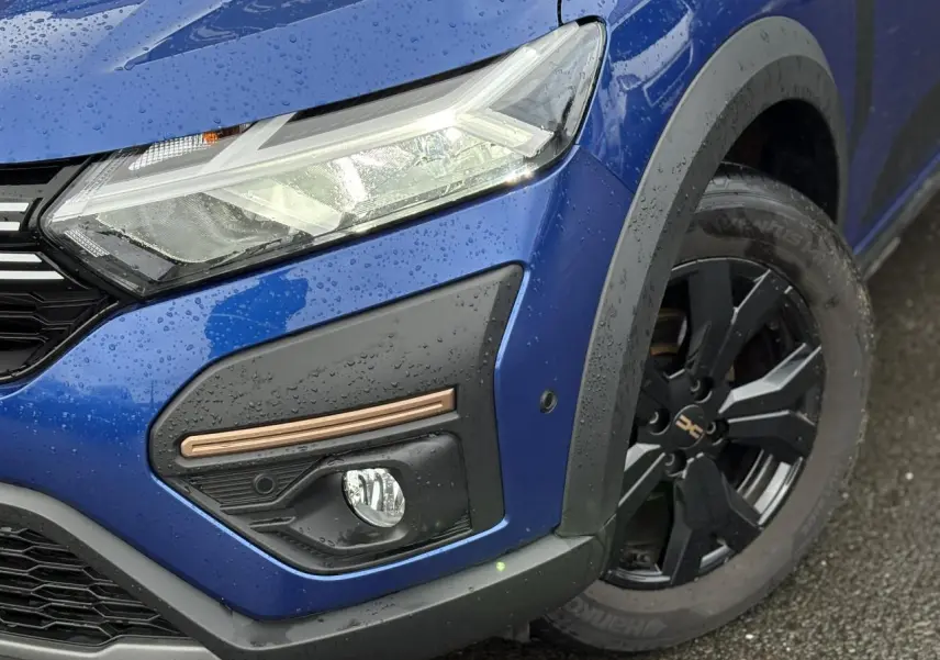 Gros plan sur l'avant droit bleu Iron du Dacia Sandero Stepway avec phare LED et jante alu noire.