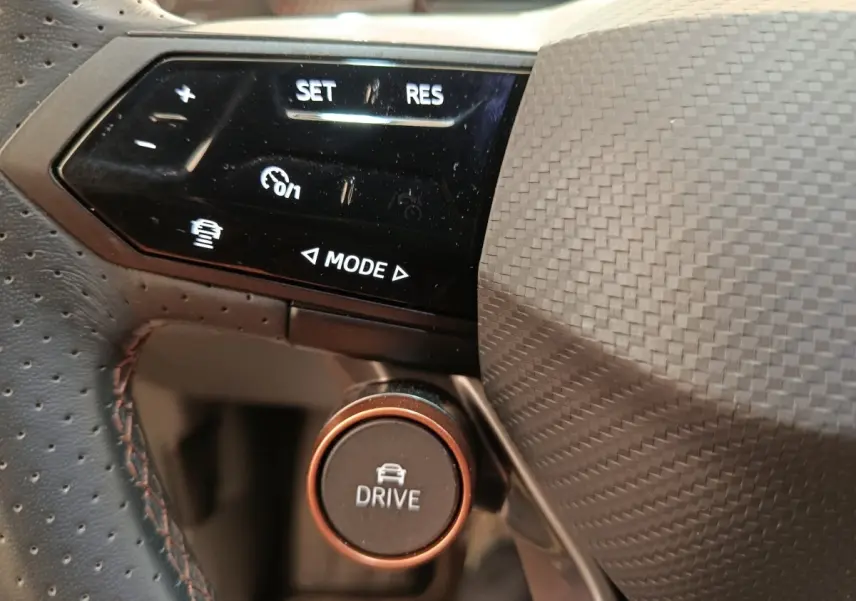 Gros plan sur les commandes du volant en cuir perforé du CUPRA BORN 230ch, bouton Drive et régulateur adaptatif visibles.