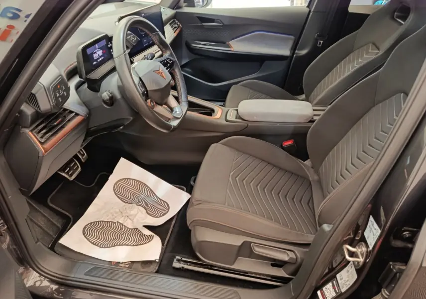 Intérieur avant droit du CUPRA BORN gris foncé 2023, sièges tissu avec surpiqûres orange et volant multifonctions cuir.