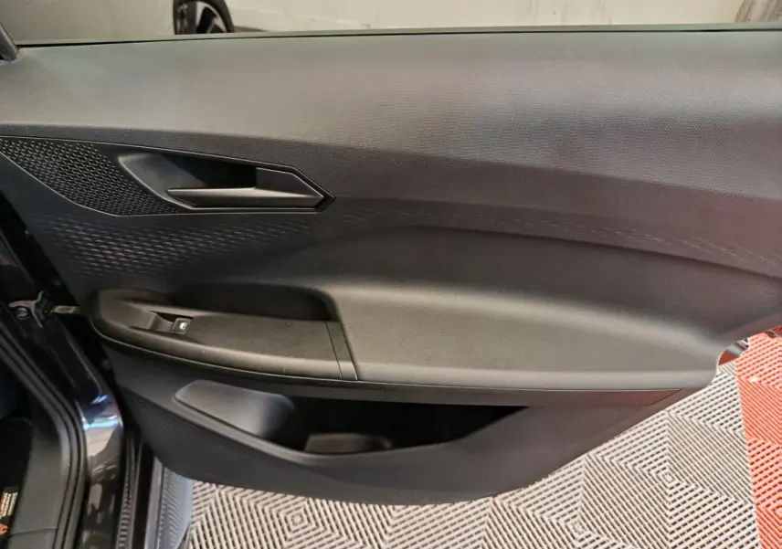 Gros plan sur la porte intérieure côté gauche d'une CUPRA BORN gris foncé, avec poignée et commande de vitre visible.
