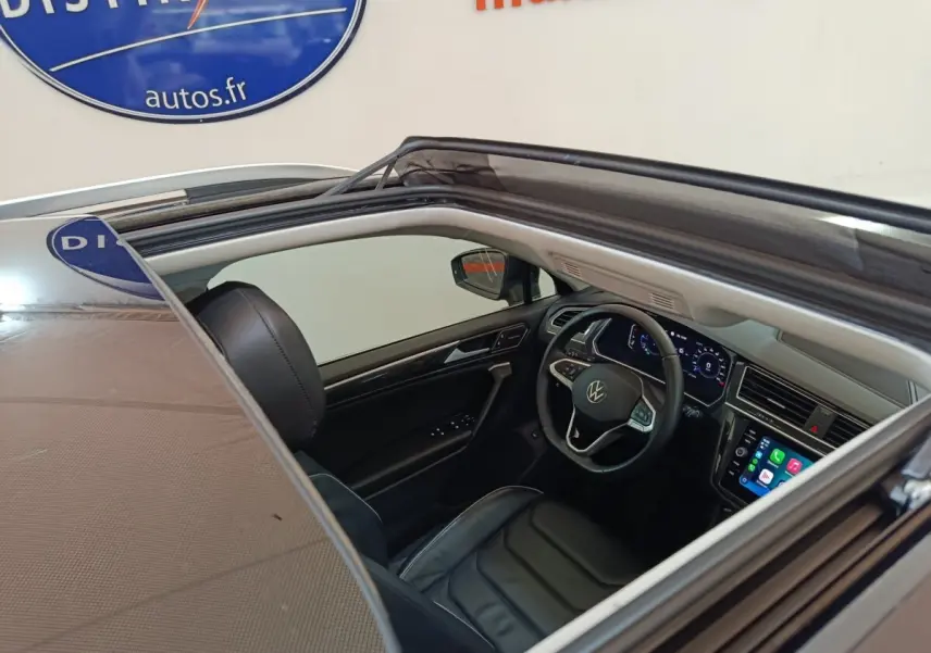 Vue intérieure côté conducteur du Volkswagen Tiguan noir 2021, volant cuir multifonctions et écran tactile visible.