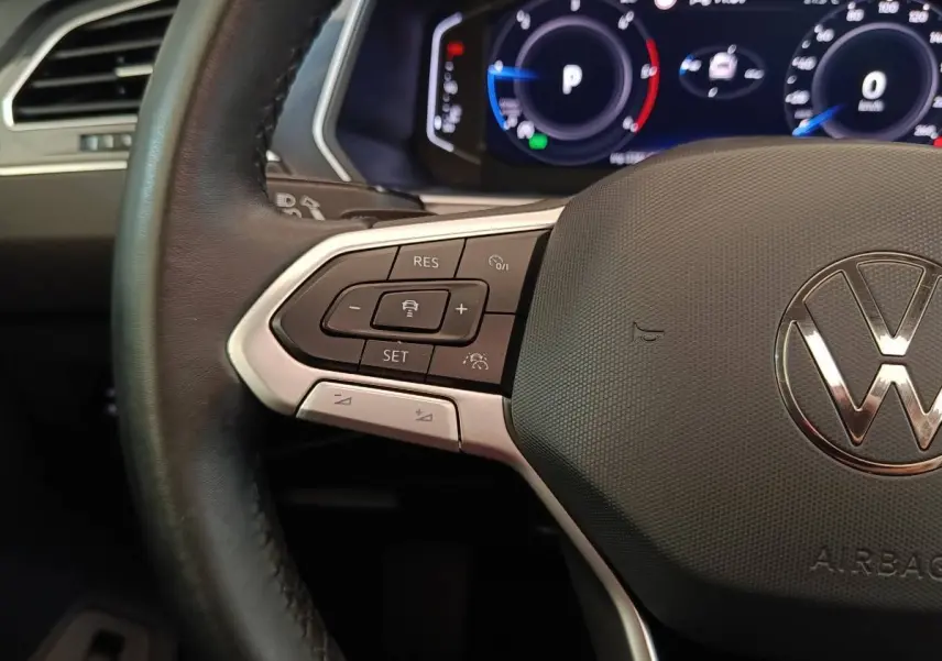 Gros plan sur le volant cuir noir du Volkswagen Tiguan 2021, avec commandes multifonctions et tableau de bord digital.