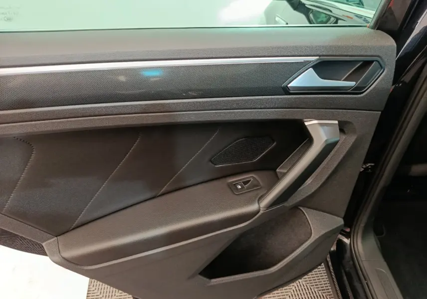 Gros plan sur la porte avant droite noire du Volkswagen Tiguan 2.0 TDI 150 DSG7 Elegance avec poignée argentée et bouton de vitre électrique.