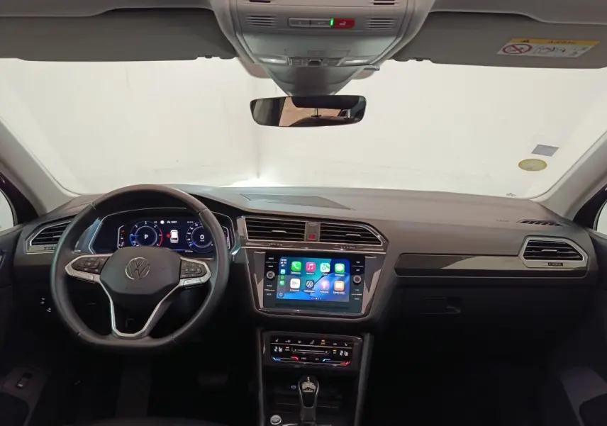 Vue intérieure frontale du Volkswagen Tiguan noir 2021, volant cuir multifonctions et écran tactile central allumé.