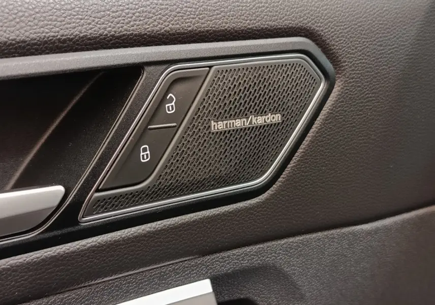 Détail intérieur montrant l'enceinte Harman Kardon et les boutons de verrouillage sur la porte noire du Volkswagen Tiguan.