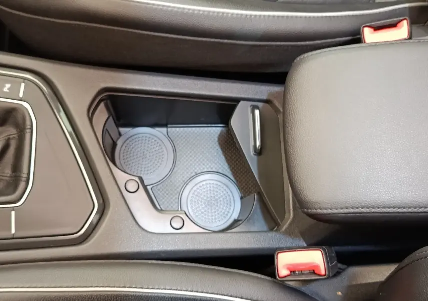 Vue rapprochée de la console centrale noire du Volkswagen Tiguan 2.0 TDI avec porte-gobelets et accoudoir cuir.