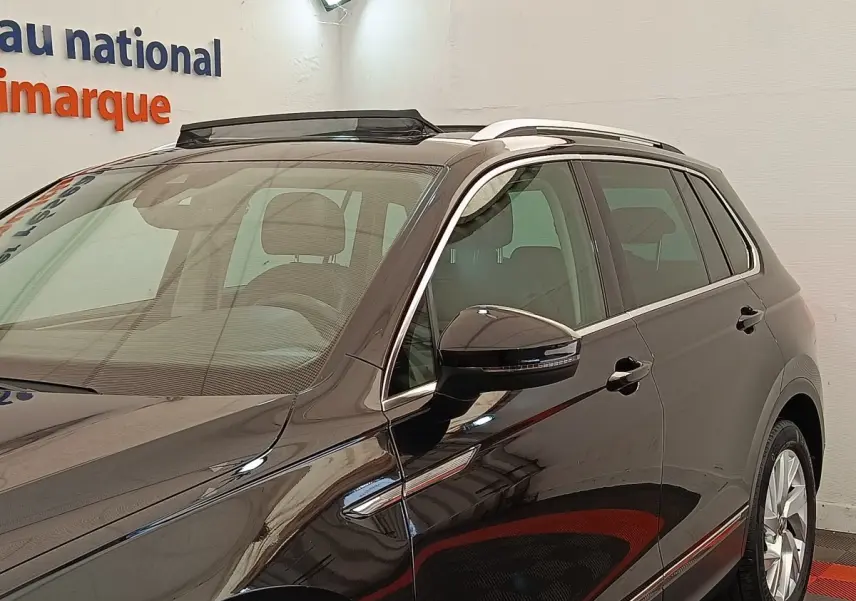 Vue 3/4 avant droit du Volkswagen Tiguan noir 2021, avec barres de toit chromées et rétroviseur droit à clignotant intégré.