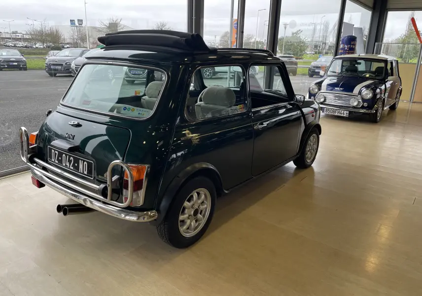 Vue 3/4 arrière droite d'une MINI 1.3 i British Open 1995 en British Racing Green avec toit ouvrant en intérieur showroom.
