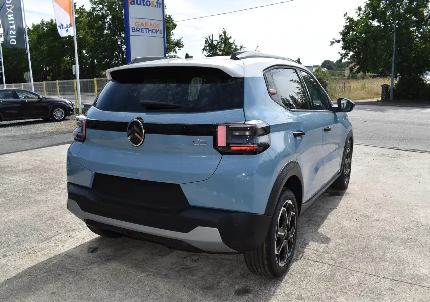 Vue 3/4 arrière droite d'une Citroën C3 2025 bleu avec toit noir et jantes biton sur parking extérieur.