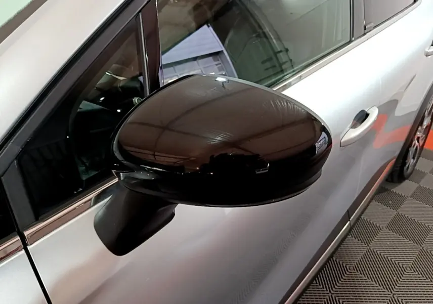 Gros plan sur le rétroviseur noir côté gauche d’un Renault Captur gris clair, vue partielle de la portière avant.