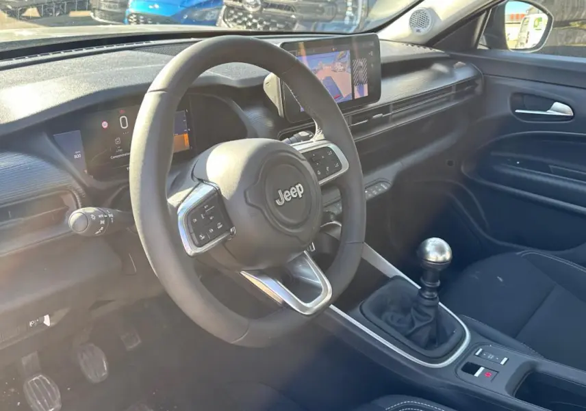 Intérieur du Jeep Avenger gris, vue côté conducteur, volant multifonction et levier de vitesse manuel visible.
