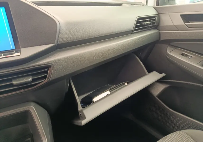Intérieur du Volkswagen Caddy 2022, vue côté passager sur la boîte à gants ouverte et tableau de bord noir.