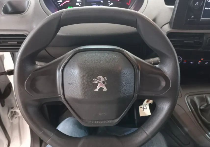 Vue rapprochée du volant noir avec logo Peugeot au centre dans l'habitacle d'un utilitaire blanc Peugeot Partner 2021.