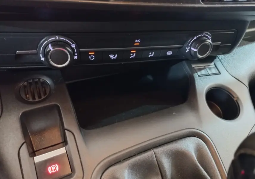 Détail intérieur du tableau de bord du Peugeot Partner blanc 2021, avec commandes de climatisation et frein à main électrique.