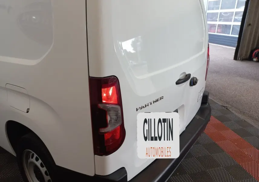 Vue arrière droite d’un Peugeot Partner blanc avec feux arrière allumés dans un garage.