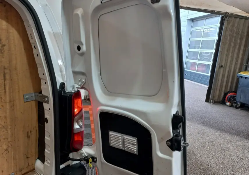Vue rapprochée de la porte arrière droite ouverte d’un Peugeot Partner blanc, montrant le feu arrière et l’intérieur du véhicule.