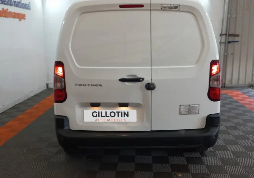 Vue arrière d’un utilitaire Peugeot Partner blanc avec feux arrière allumés dans un garage.