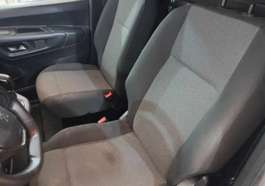 Vue intérieure côté conducteur du Peugeot Partner 2021, sièges tissu gris et noir avec volant partiellement visible.
