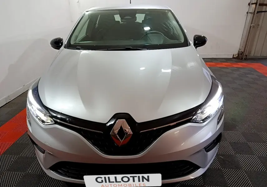 Vue avant d'une Renault Clio gris clair 2023 avec phares LED allumés dans un garage.