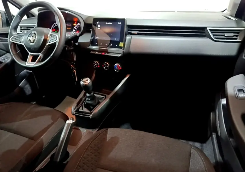 Vue intérieure côté conducteur de la Renault Clio gris clair 2023, volant cuir, écran tactile central et boîte manuelle.