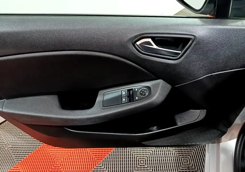 Vue rapprochée de la porte avant gauche de la Renault Clio gris clair, avec commandes électriques des vitres et poignée intérieure noire.