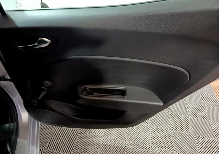 Vue rapprochée de la porte intérieure côté gauche d’une Renault Clio gris clair 2023 avec poignée noire et manivelle de vitre.