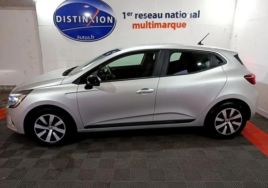 Profil droit d'une Renault Clio Equilibre TCe 90 gris clair 2023, avec jantes stylisées et feux arrière allumés.