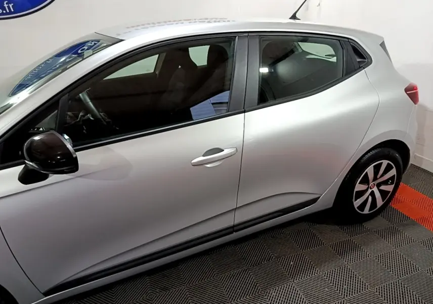 Profil côté gauche de la Renault Clio Equilibre TCe 90 gris clair, avec rétroviseur noir et jantes stylisées visibles.