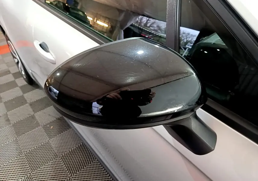 Gros plan sur le rétroviseur noir côté gauche d'une Renault Clio gris clair, vue partielle de la portière avant.