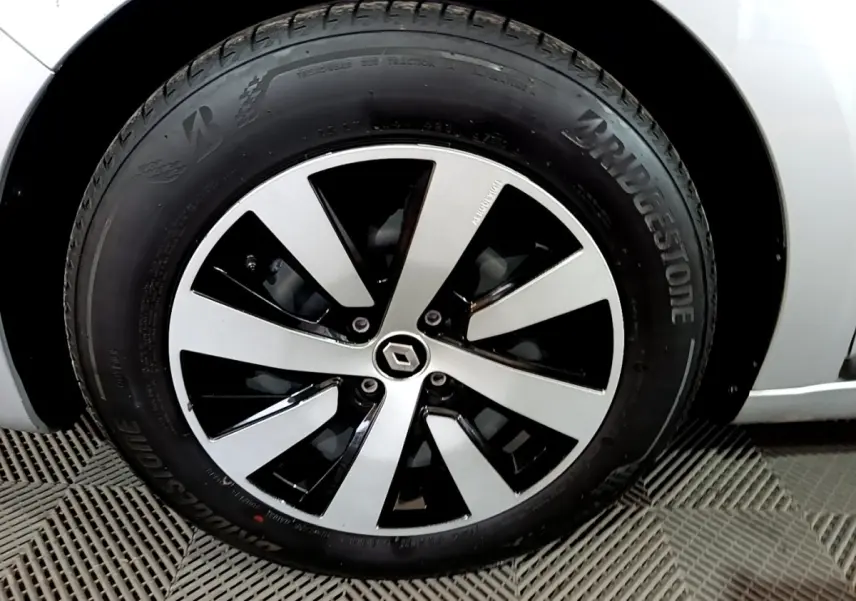 Gros plan sur la roue avant gauche d'une Renault Clio gris clair avec jante alliage bicolore et logo Renault central.