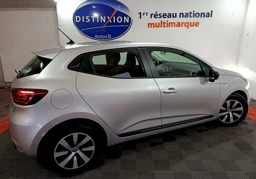 Profil droit de la Renault Clio 2023 gris clair, avec jantes noires et grises, stationnée en intérieur sur sol carrelé.