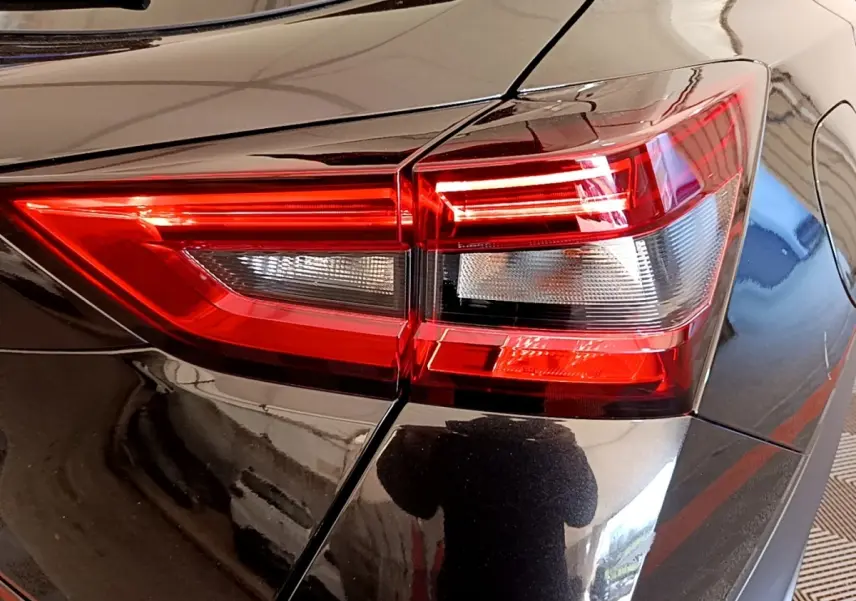 Gros plan sur le feu arrière droit rouge et blanc d’un Nissan Juke noir brillant, reflet de l’environnement visible.