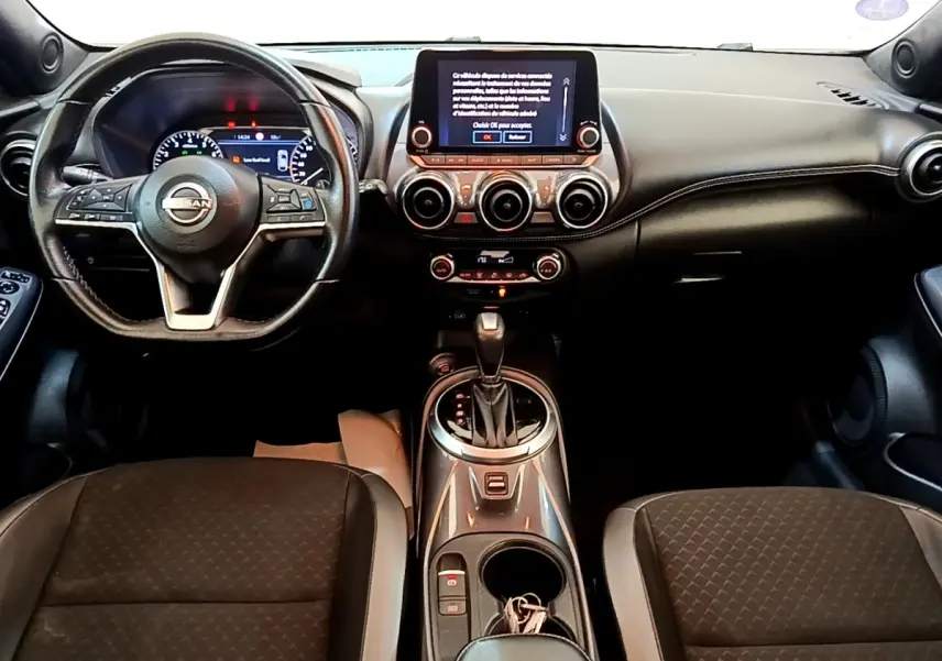 Vue intérieure avant du Nissan Juke noir 2022, tableau de bord avec écran tactile central et volant multifonctions.