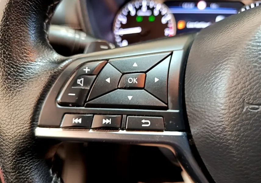 Gros plan sur les commandes gauche du volant noir du Nissan Juke 2022 avec tableau de bord lumineux en arrière-plan.