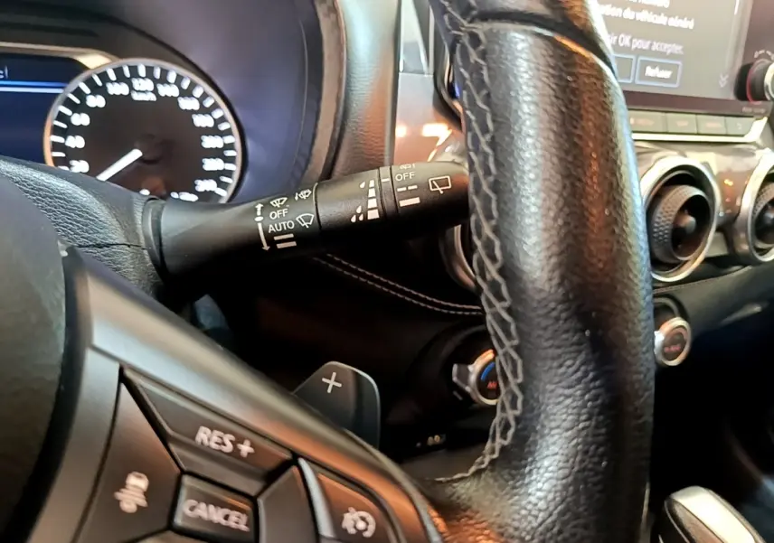 Vue rapprochée du volant noir du Nissan Juke 2022, montrant les commandes multifonctions et le tableau de bord lumineux.