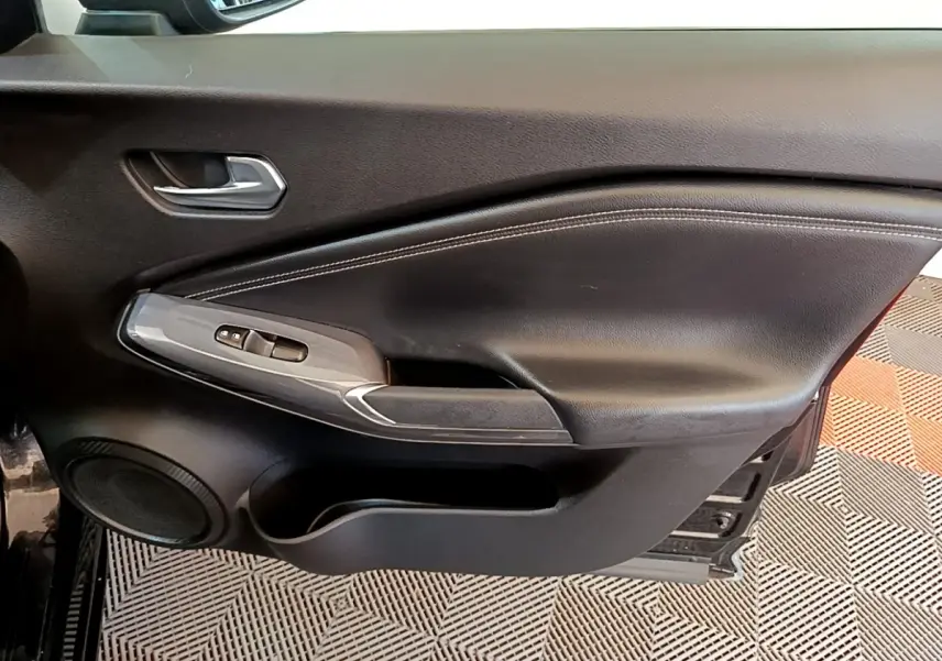 Vue intérieure du panneau de porte côté conducteur noir avec commandes des vitres et haut-parleur intégré sur Nissan Juke 2022.